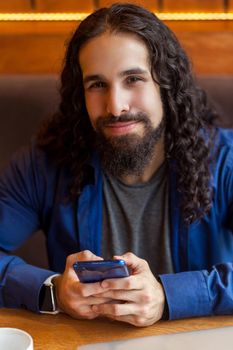 Close up portrait of cheerful handsome intelligence young adult man freelancer in casual style sitting in cafe, holding phone and looking at camera, bussinessman in office. Indoor, lifestyle concept