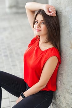 beautiful woman in casual style clothes sitting near grey column at street. outdoor shot