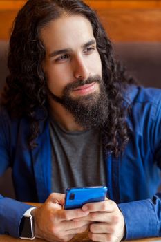 Close up portrait of cheerful handsome intelligence young adult man freelancer in casual style sitting in cafe, holding phone and looking away, bussinessman in office. Indoor, lifestyle concept