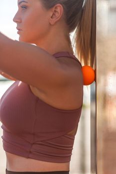 Closeup young woman shoulders in tight top leaning on small ball against wall to fix back ache, massaging stiff muscles and sore neck, exercise to relieve spinal pain. Relaxation and muscle stretching