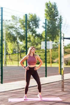Positive fit athletic woman in tight pants warming up on mat outdoor summer day, doing aerobics or pilates exercise, workout routine, smiling feeling happiness and energy to practice sports activity