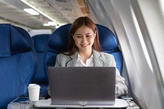 Traveling and technology. Flying at first class. Pretty young asian businees woman working on laptop computer while sitting in airplane.