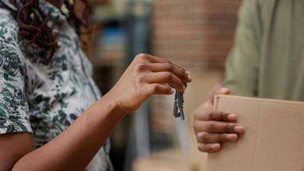 African american homeowners holding house keys and boxes to move in new apartment flat, buying first property together. Celebrating real estate investment. Handheld shot. Close up.