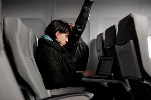 Young adult working on laptop during airplane flight abroad, using online internet on computer to travel to holiday destination. Tourist waiting to arrive after commercial flight transportation trip.