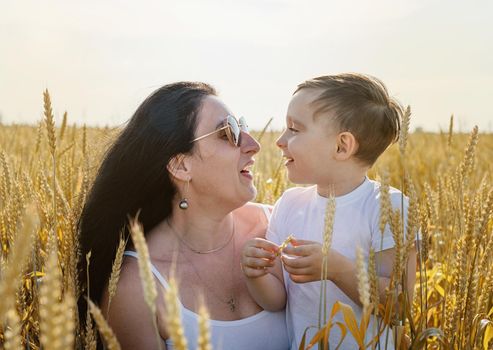 Happy family on a summer walk, mother and child walk in the wheat field and enjoy the beautiful nature, at sunset