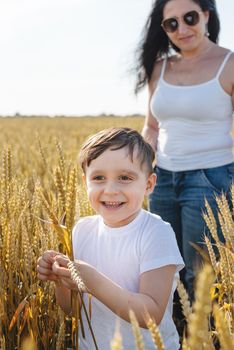 Happy family on a summer walk, mother and child walk in the wheat field and enjoy the beautiful nature, at sunset