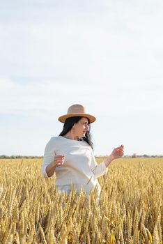 Mid adult woman in white dress walking and dancing across golden field holding heap of rye lit by sunset light, copy space