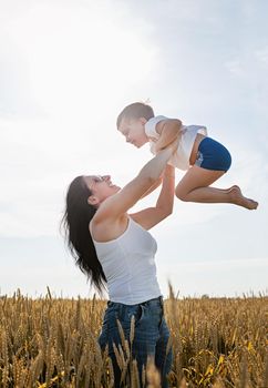 Happy family on a summer walk, mother and child walk in the wheat field and enjoy the beautiful nature, mom pick up child