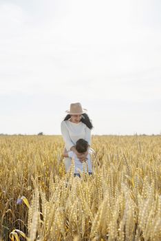 Happy family on a summer walk, mother and child walk in the wheat field and enjoy the beautiful nature, at sunset