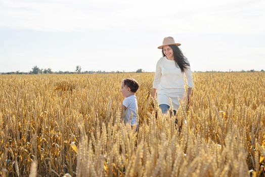 Happy family on a summer walk, mother and child walk in the wheat field and enjoy the beautiful nature, at sunset