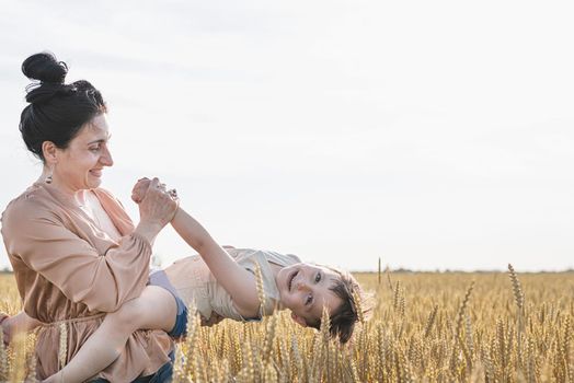 Happy family on a summer walk, mother and child walk in the wheat field and enjoy the beautiful nature, at sunset