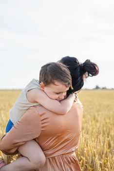 Happy family on a summer walk, mother and child walk in the wheat field and enjoy the beautiful nature, at sunset, hugging and kissing