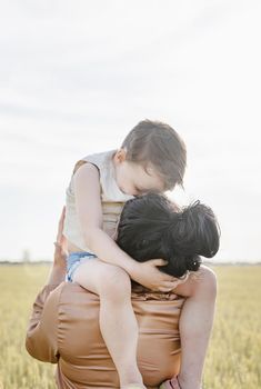 Happy family on a summer walk, mother and child walk in the wheat field and enjoy the beautiful nature, at sunset, hugging and kissing