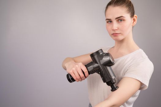 Caucasian woman uses a massager gun for pain in the muscles of the arm