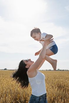 Happy family on a summer walk, mother and child walk in the wheat field and enjoy the beautiful nature, mom pick up child