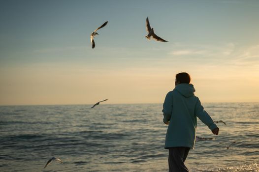 Caucasian woman feeding seagulls at sunset by the sea