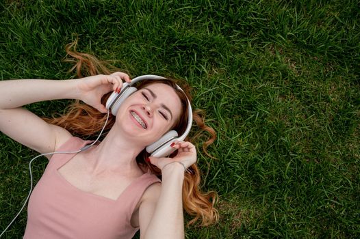 A young red-haired woman lies on the grass and listens to music