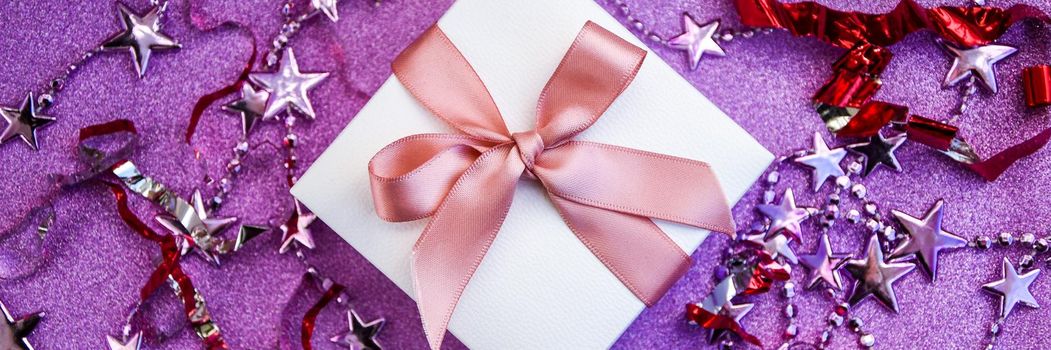 banner for Merry Christmas or St Valentines Day card made of decorations, white gift boxes with pink ribbon, sparkles and confetti on purple and pink background. Holiday concept