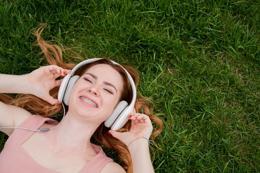 A young red-haired woman lies on the grass and listens to music