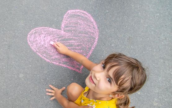 The child draws a heart on the asphalt with chalk. Selective focus. Kid.