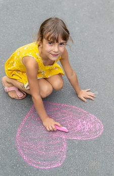 The child draws a heart on the asphalt with chalk. Selective focus. Kid.