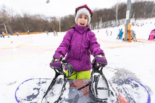 little cute girl learning to ride a children's snowboard, winter sports for the child, safety of active sports