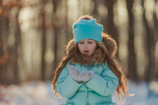 little girl blows on the snow that is on her mittens