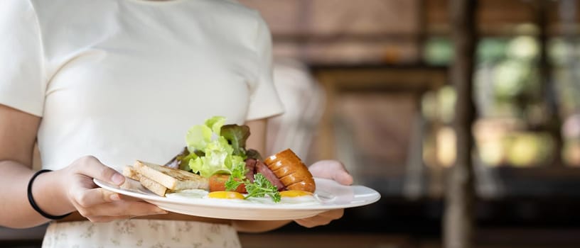 Young woman holding plate with fried eggs, roasted bacon, toasts, sausages and fresh salad for healthy breakfast.