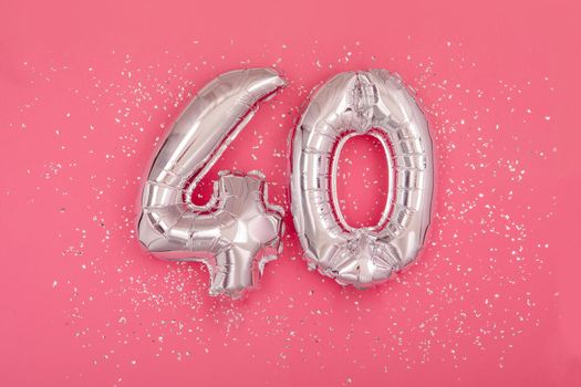 Silver balloon number 40 fourty shape sparkles scattered randomly on juicy pink background. Silver confetti pink background
