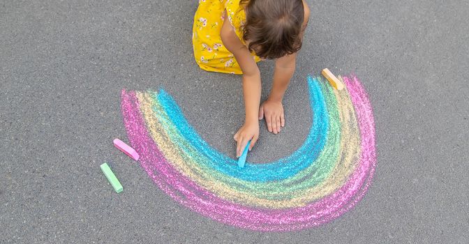 A child draws a rainbow on the asphalt. Selective focus. kid.