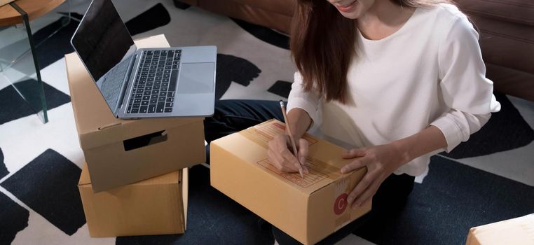 Shipping shopping online ,young start up small business owner writing address on cardboard box at workplace.small business entrepreneur SME or freelance asian woman working with box at home.