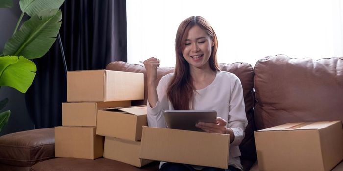 Happy young Asian woman entrepreneur, Smile for sales success after checking order from online shopping store in a laptop at home office, Concept of merchant business online and eCommerce.