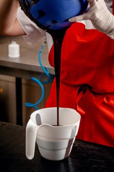 A woman confectioner with red uniform and white sterile gloves preparation of black designer candies. Preparation of chocolate glaze decorations for candy.