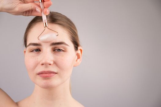 Close-up portrait of a woman uses a quartz roller massager to smooth wrinkles on her forehead