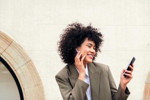 happy woman with wireless earphones enjoys making a video call outdoors with her phone, concept of youth and technology, copy space for text