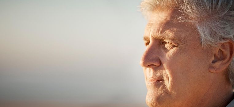 Mature man enjoying the view on the beach. Senior man looking at the view on the beach. Mature man on holiday by the beach. Closeup on face of older man enjoying a holiday on the beach