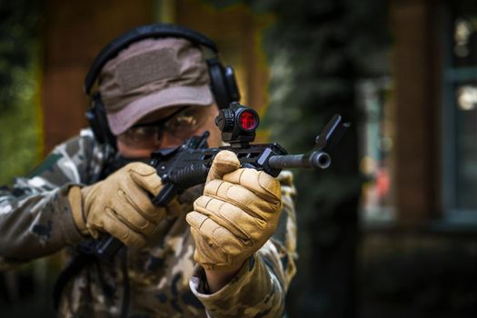 Man with a gun in military uniform tactical hearing protector headset. Police training in shooting gallery with weapon. Civil police man in tactical training course. Selective focus on hand.