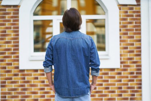 Back view of a man standing alone looking at old town building while traveling in european cities during vacation time wearing denim. Travel concept.