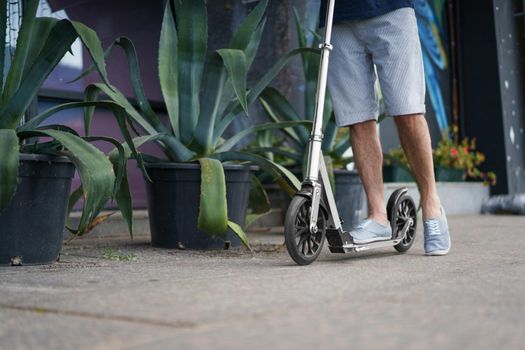 Close up of man feet stand on town adult scooter with big wheels in a stylish sneakers having a ride on the streets or park after work outdoors. No face visible. Selective focus on front wheel.