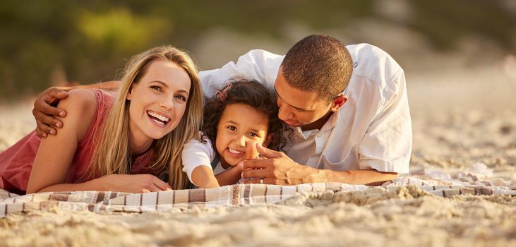 Portrait of a happy mixed race family spending time together on the beach. Adorable little girl enjoying vacation with her mother and father.