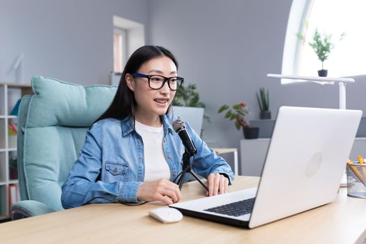 Young beautiful Asian woman recording audio podcast, woman in office using professional microphone.