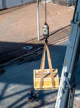 The crane carrying a wooden box of the radioactivity instrument holder transportation wooden box and A worker riding a bicycle on the ground