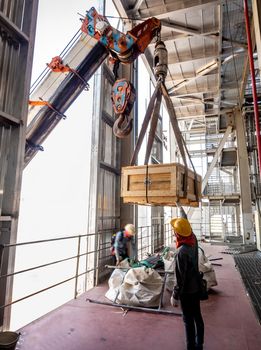 The crane carrying a wooden box of the radioactivity holder into the window on the factory floor