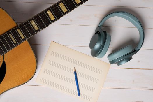 Music recording scene with guitar, empty music sheet, pencil and headphones on white wooden table