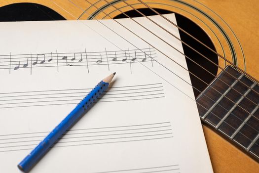 Music recording scene with guitar, music sheet and pencil on wooden table