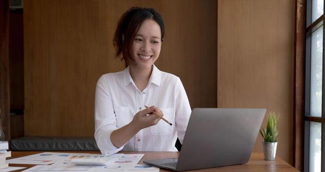 Pretty asian woman fiddling with pen and thinking over a subject while sitting in some coffee shop with her laptop, location public..