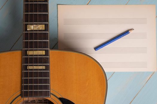 Music recording scene with guitar, empty music sheet and pencil on wooden table