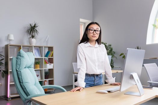 Successful Asian business woman at workplace in office looking at camera, portrait of strong leader.