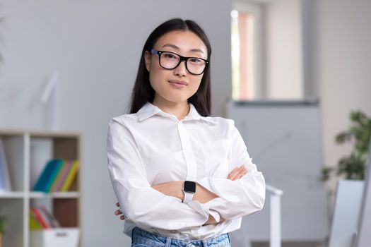 Portrait of a young Asian business woman, a worker in the office with crossed arms looking at the camera.