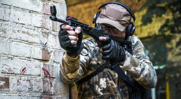 Young man with gun standing sideways near brick wall during advanced firearms, defense tactics, use of force policy review, officer safety updates. In-service training cycle for civil police troops.